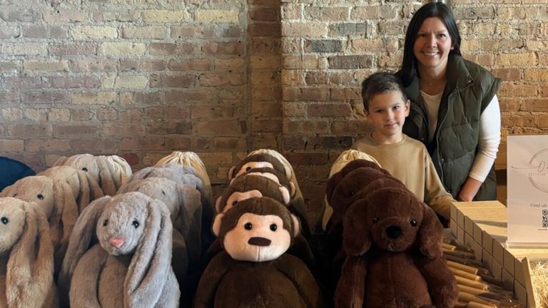 A mom and her child stand behind a display of plush sensory toys, including bunnies, monkeys, and dogs.