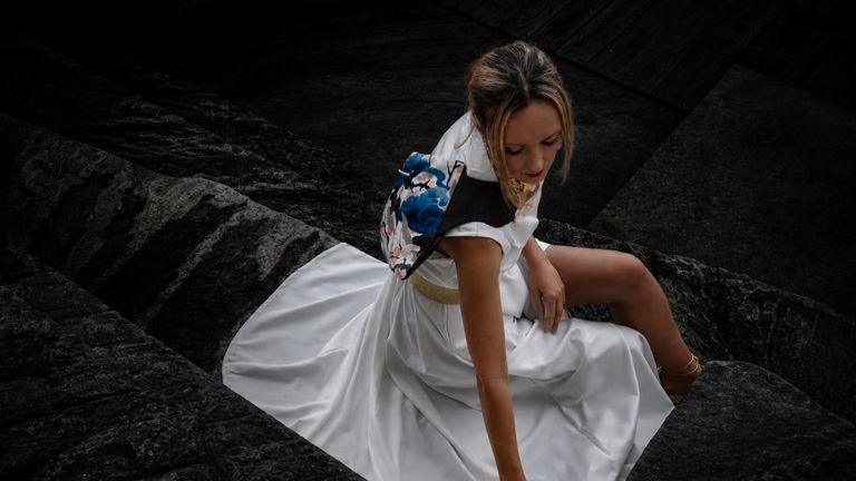 Woman in white dress carrying patterned lvb_collection bag while seated on dark stone steps.
