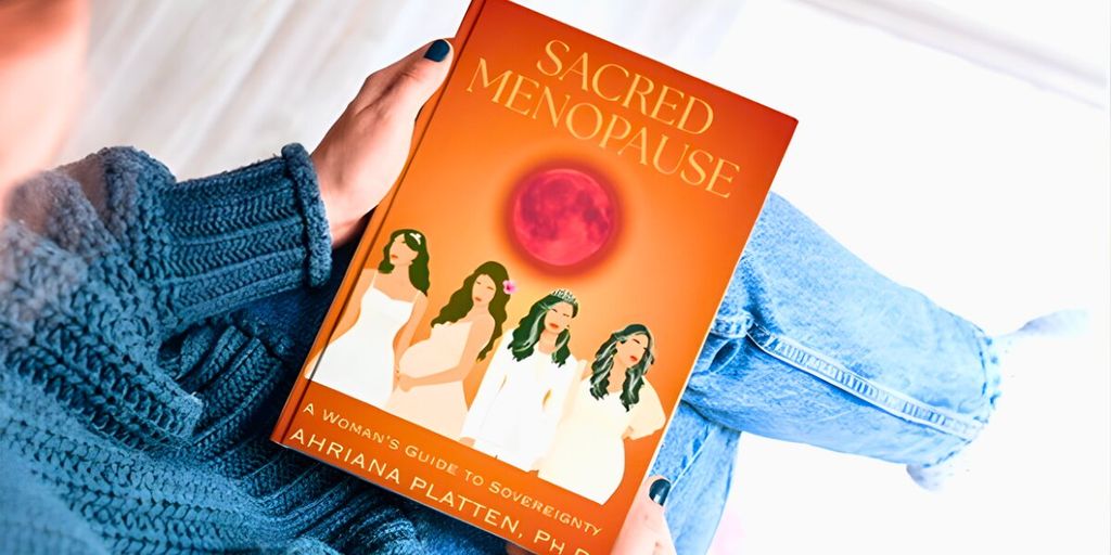 A person holding the book Sacred Menopause by Dr. Ahriana Platten, featuring a colorful cover and empowering message.