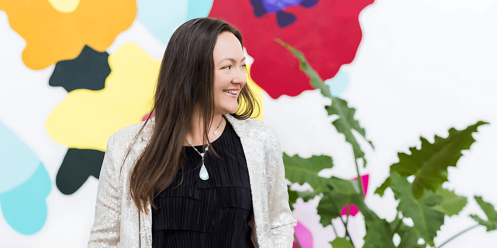 Jessie Perez smiling in front of colorful mural, representing her joyful, transformative approach to healing and reconciliation.