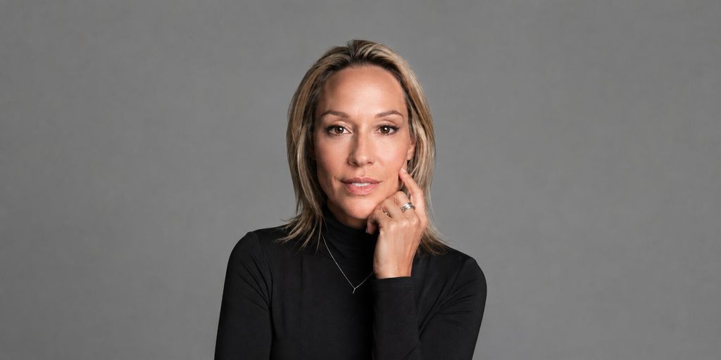 Coach Julianne wearing a black turtleneck in a professional studio portrait against a gray background.