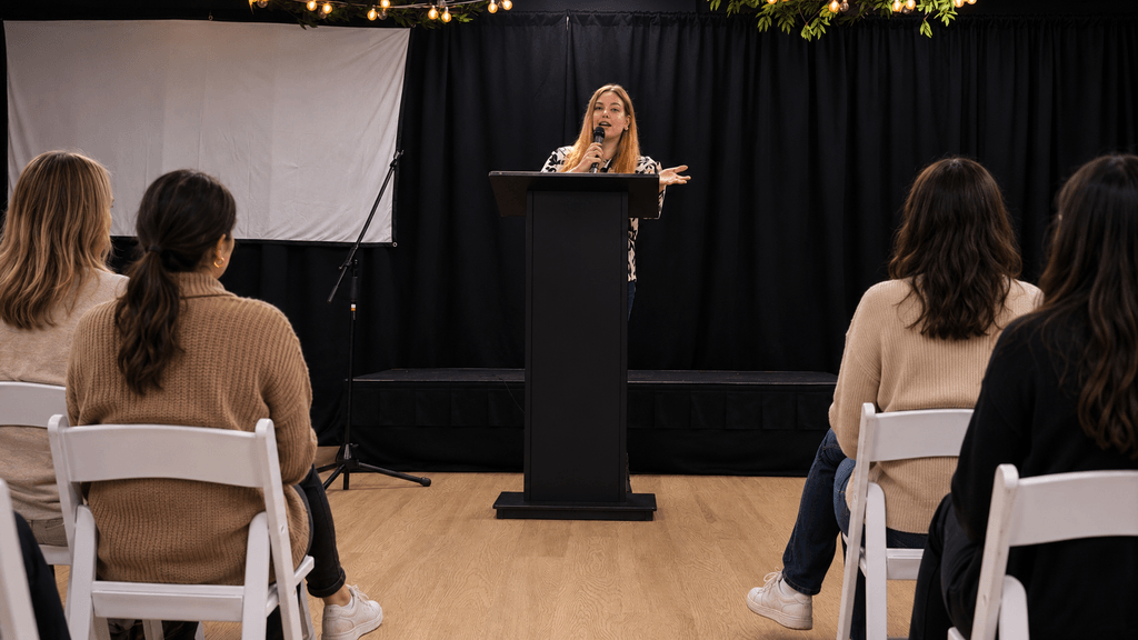 Woman speaking at a podium during a women’s empowerment or storytelling event.