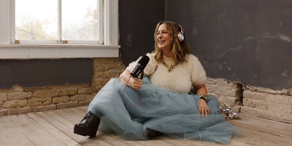 Kimberly Spencer seated with headphones and microphone, speaking in a relaxed podcast-style setting.