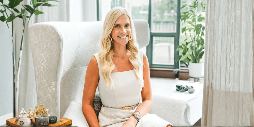 Sara Lewis Hartley smiling while seated in a calming, light-filled space promoting emotional wellness.
