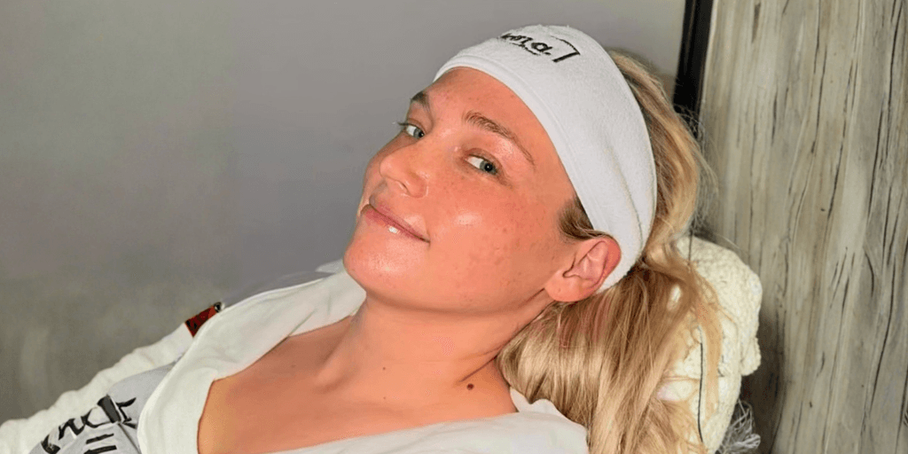 Woman wearing headband reclines during facial treatment, glowing skin in serene spa setting.