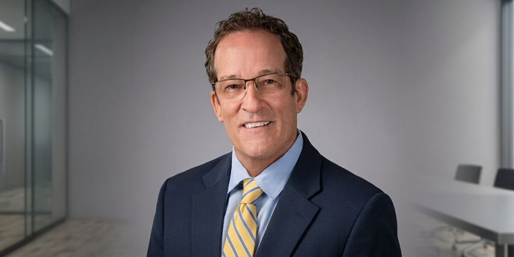 Professional headshot of financial advisor in navy suit and yellow striped tie in modern office.