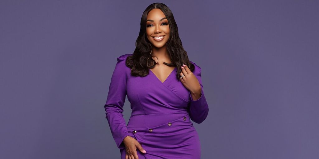Portrait of Dr. Monica Moray smiling in a purple dress against a solid purple background.