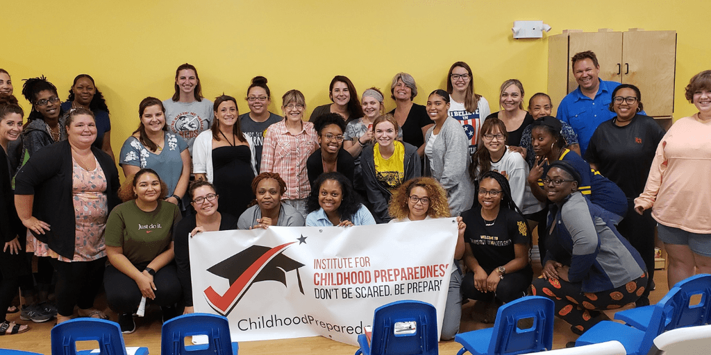 "A group photo of diverse individuals smiling and posing together with a banner from the Institute for Childhood Preparedness, promoting the message 'Don't Be Scared. Be Prepared'."