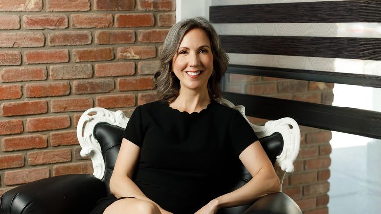 Smiling orthodontist seated in elegant office with brick wall background.