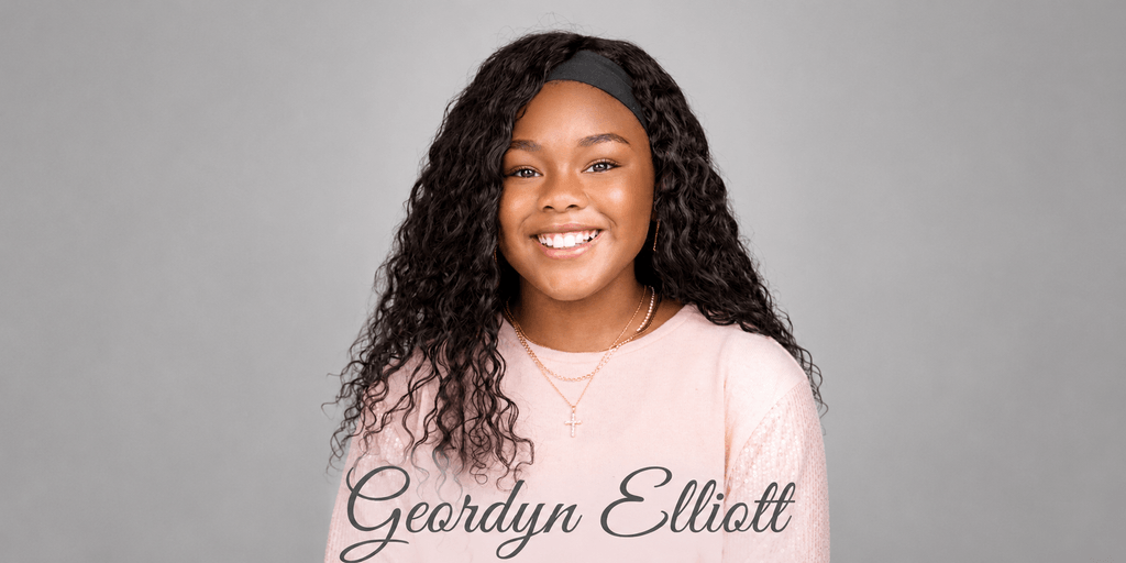 Smiling young author Geordyn Elliott wearing a pink shirt and cross necklace against a gray background.