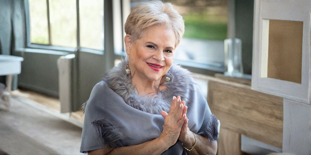 Elaine Adita Agnes smiling warmly, dressed in a chic, fur-trimmed gray shawl, radiating confidence and authenticity.