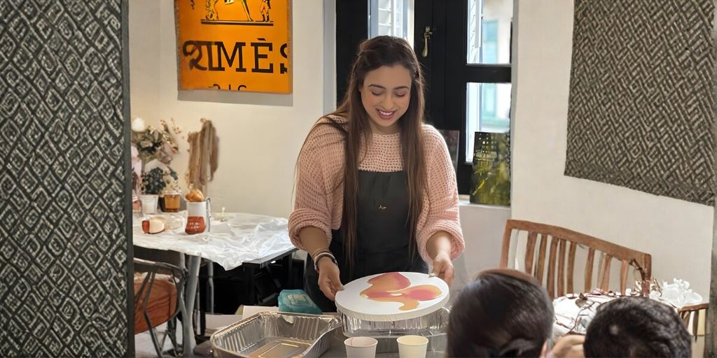 A woman smiling as she presents a painted circular artwork to others in a warm, creative environment.