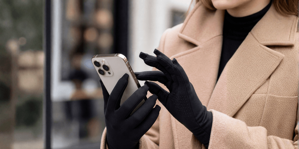 Woman using smartphone while wearing black touchscreen gloves outdoors.