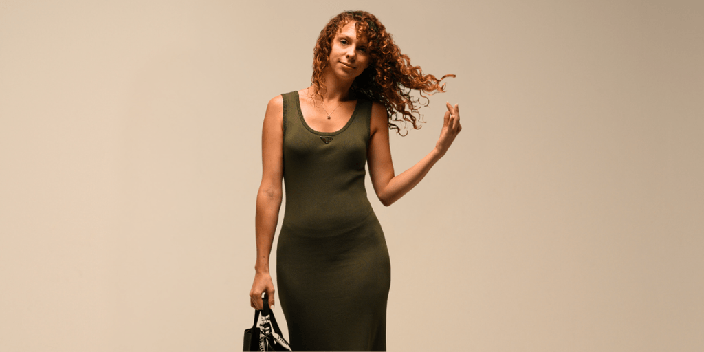 A confident woman in a green dress, holding a handbag, with curly hair flowing.