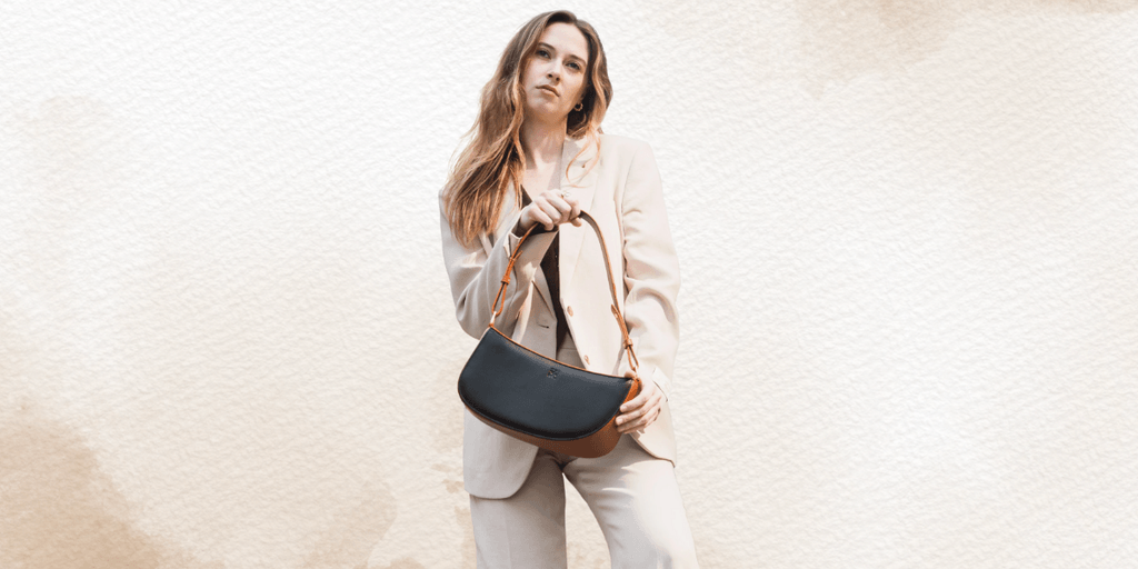 A woman in a beige suit holding a stylish black and brown handbag, standing against a soft, neutral background.
