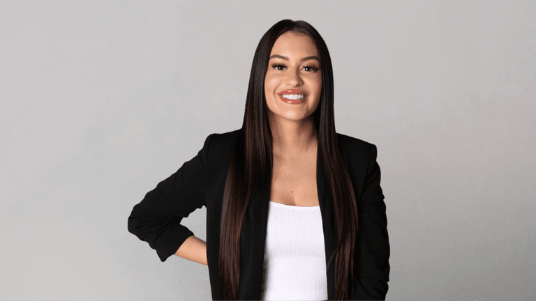 Erica Battista smiling in a black blazer against a neutral gray background.