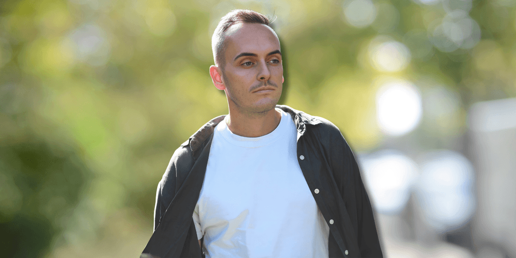 Man walking outdoors on a sunny day with trees and a blurred background.