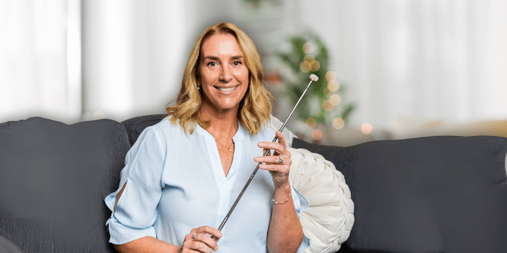 Smiling woman sitting on a couch holding a long metal pointer in a softly lit living room.