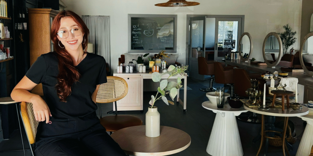 A woman smiles in a modern salon with stylish decor and a cozy, welcoming atmosphere.