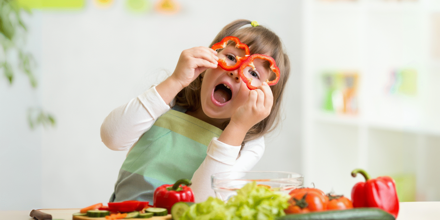 Before They Turn 3: The 3 Habits That Shape a Lifetime of Healthy Eating Child holding red bell pepper slices as glasses while smiling.