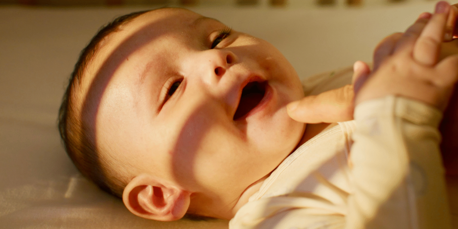 Baby smiling while lying down, with light and shadow patterns on their face.