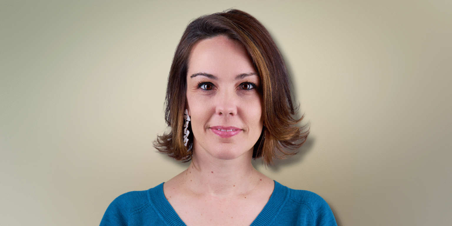 A close-up portrait of a woman in a teal sweater with a neutral background.