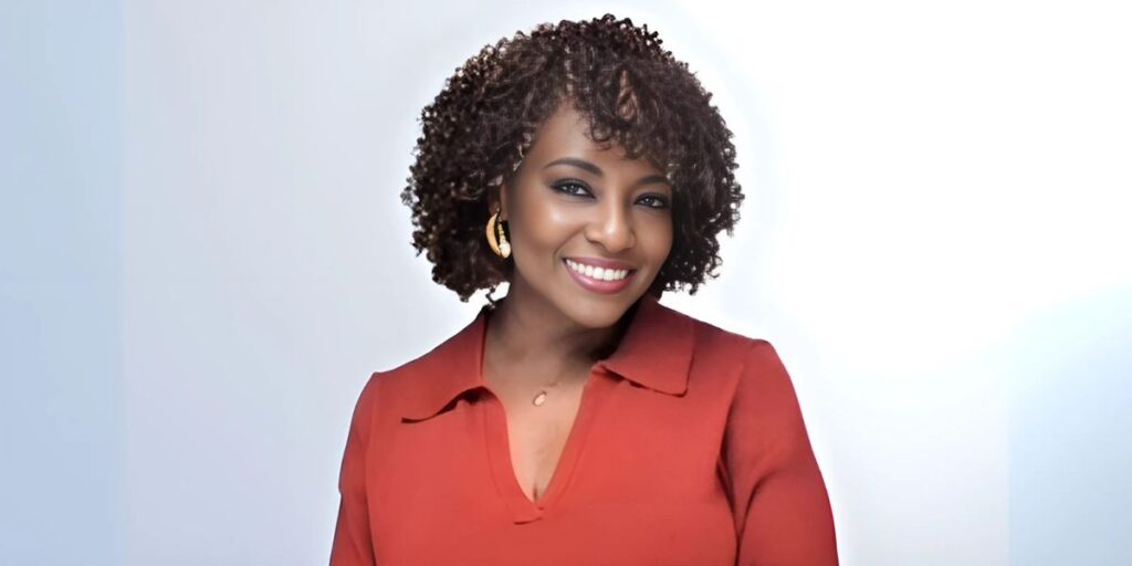 "A woman with curly hair in a red dress smiling at the camera in front of a clean, minimal background."
