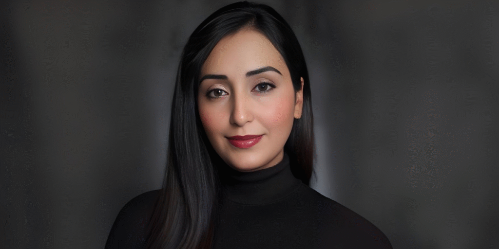 "Portrait of a woman with long black hair and neutral makeup, wearing a black turtleneck top, exuding a professional and confident look against a blurred background."