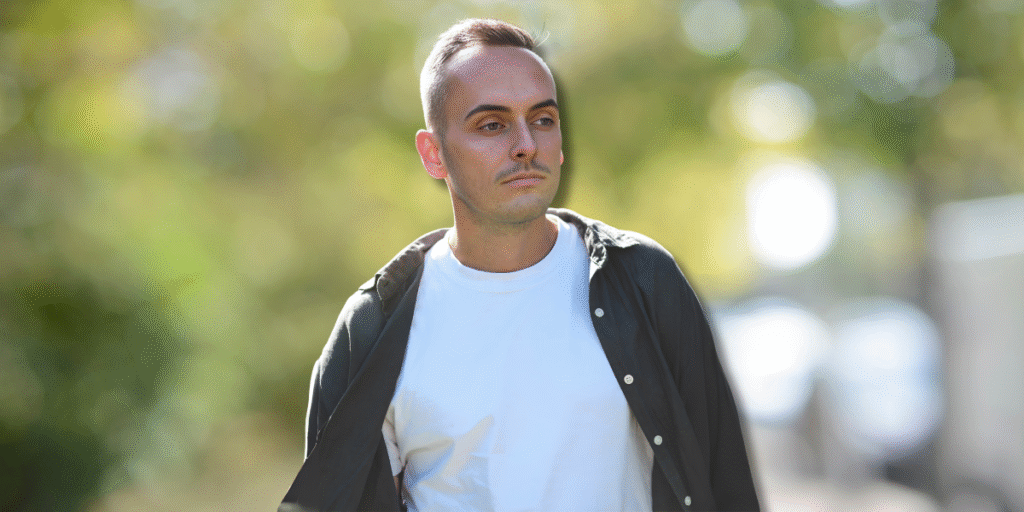 Man walking outdoors on a sunny day with trees and a blurred background.