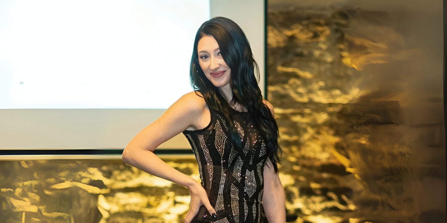 Woman in a black sequined dress posing confidently in front of a presentation screen and textured wall.
