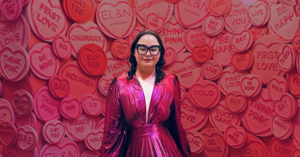 Woman in pink dress stands before heart-themed wall at EL&N London, representing healing and empowerment from heartbreak.