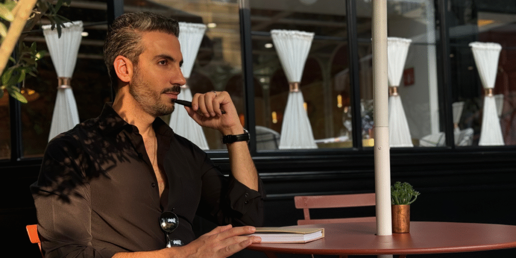 "Johnny Abraham, relationship mentor and author, reflects thoughtfully at an outdoor café, embodying his teachings of emotional growth."