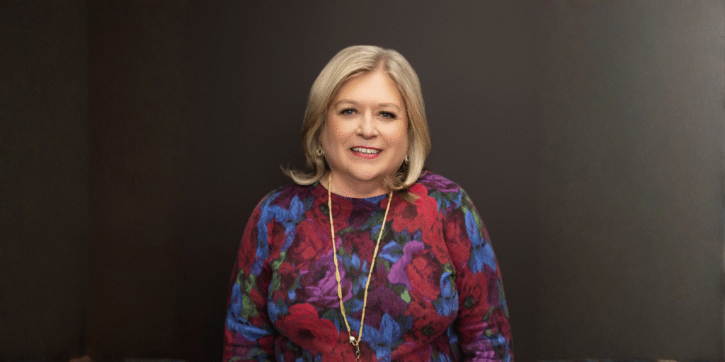 Marcy Westcott, meditation teacher and author, smiling in a colorful floral sweater against a dark background.