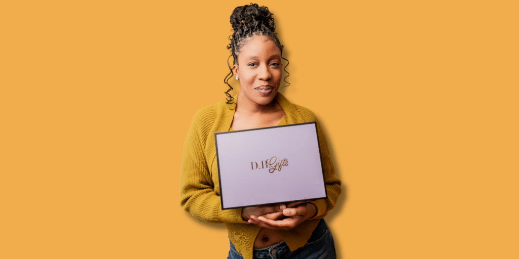 "Smiling woman wearing a yellow sweater, holding a lavender gift box with the D.B. Gifts logo, set against a bright orange background."