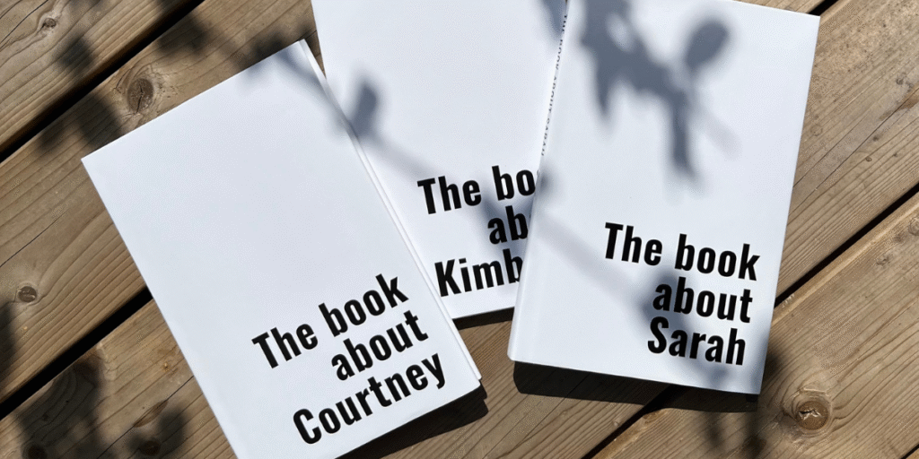 Three personalized hardcover books titled "The book about Courtney," "Kimberly," and "Sarah" on a wooden surface.
