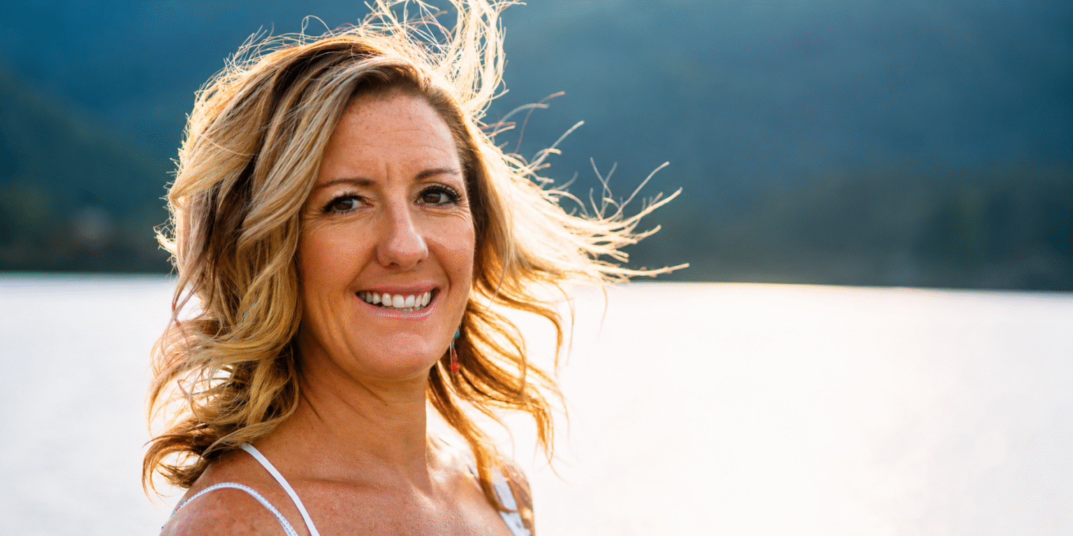 The Menopause Strategist: How Marjie Martini Is Redefining Midlife Through Strategy, Sovereignty, And Reinvention Marjie Martini smiling outdoors beside a lake with mountains in the background.