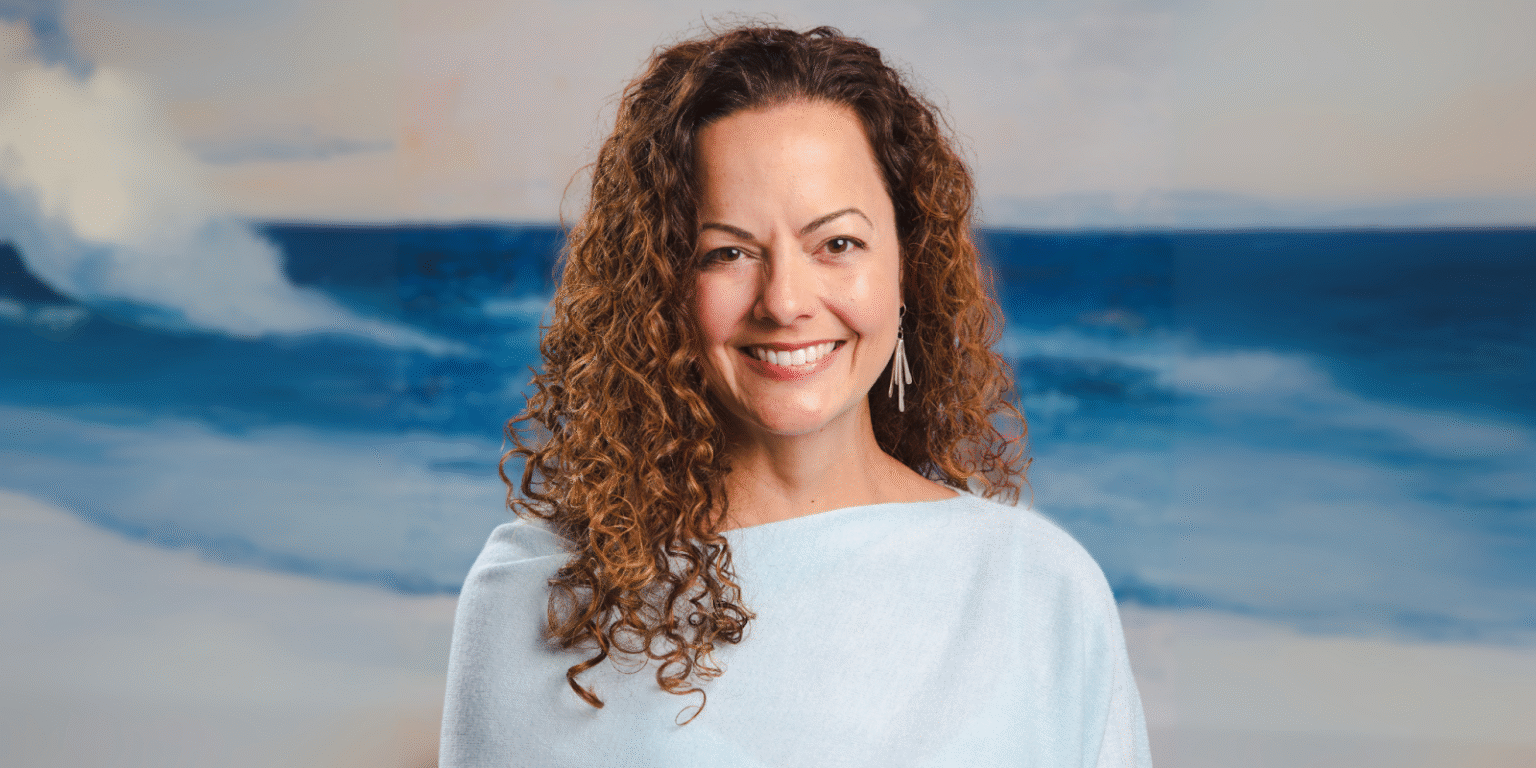 Julie Speetjens smiling in front of ocean background, representing her healing work with Empaths through Reiki and intuition.