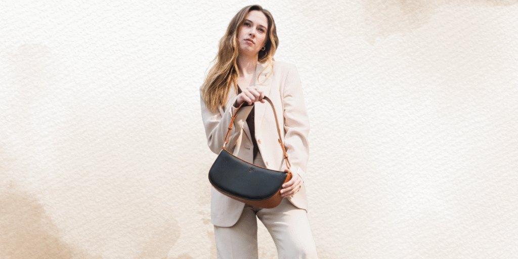A woman in a beige suit holding a stylish black and brown handbag, standing against a soft, neutral background.