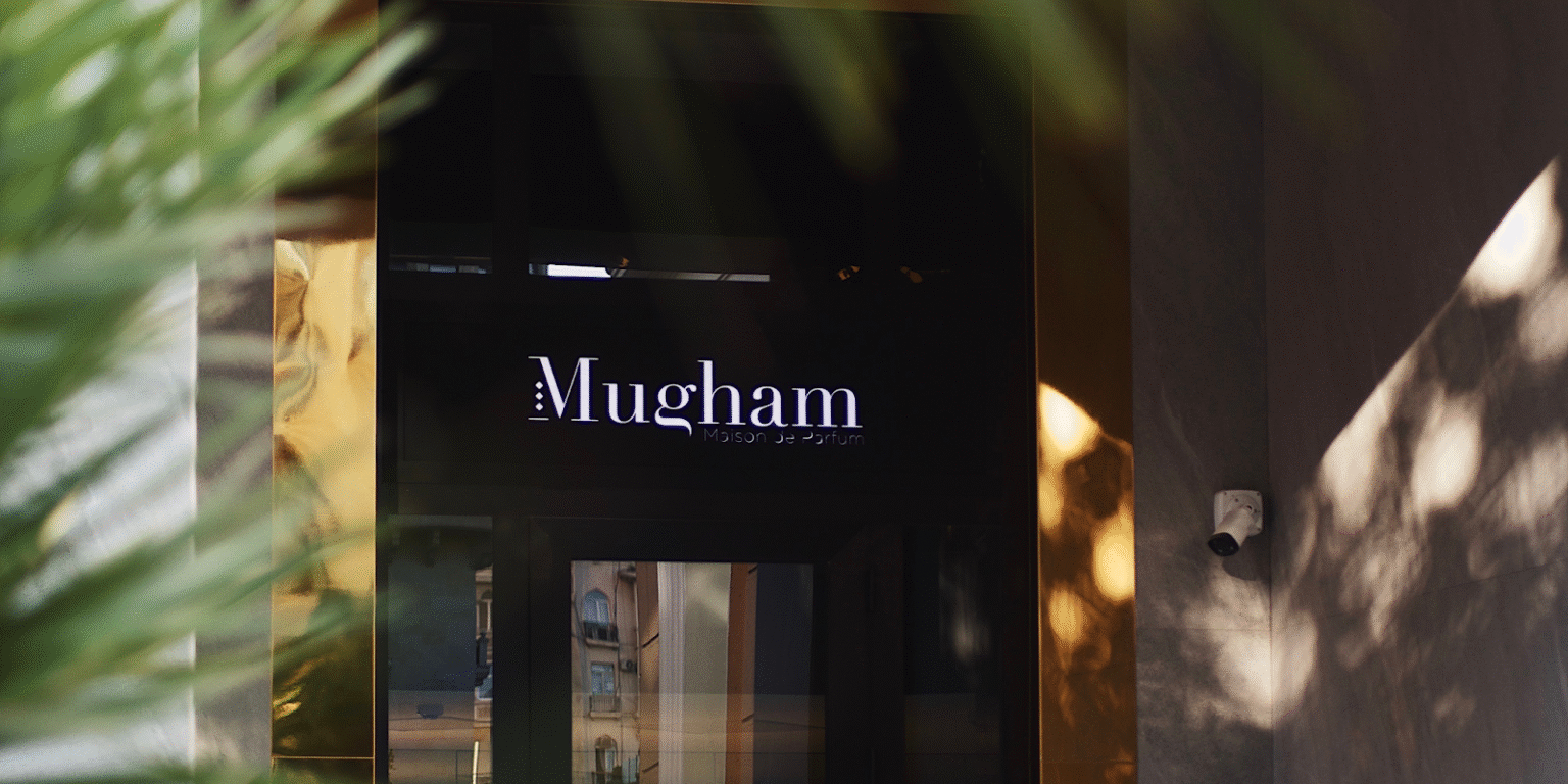 Elegant entrance of Maison Mugham, showcasing the brand's name under soft lighting, framed by golden accents and palm leaves.