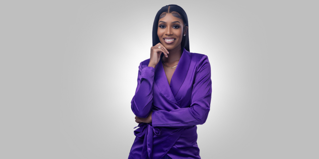 Ashmara Lawrence, a financial coach, smiles confidently in a purple blouse, empowering women to build generational wealth.