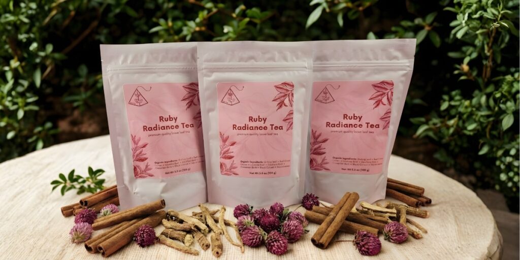 Three resealable pouches of Ruby Radiance Tea arranged on a wooden surface, surrounded by dried cinnamon, licorice root, and clover.