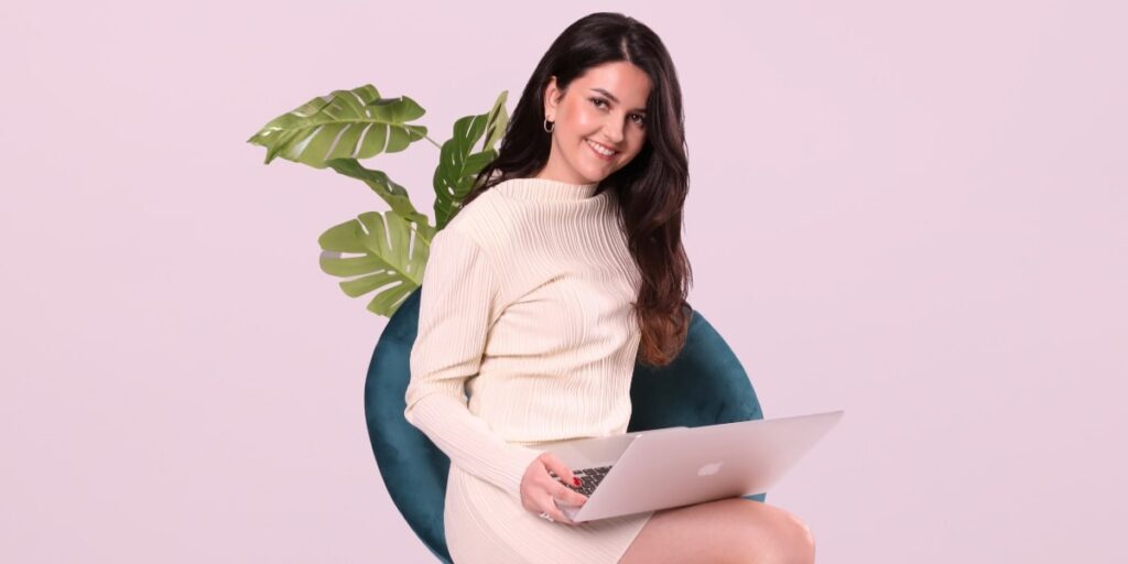 Danin Bozovic, founder of Lux & Class, smiles confidently while sitting with a MacBook, showcasing modern, empowering style."