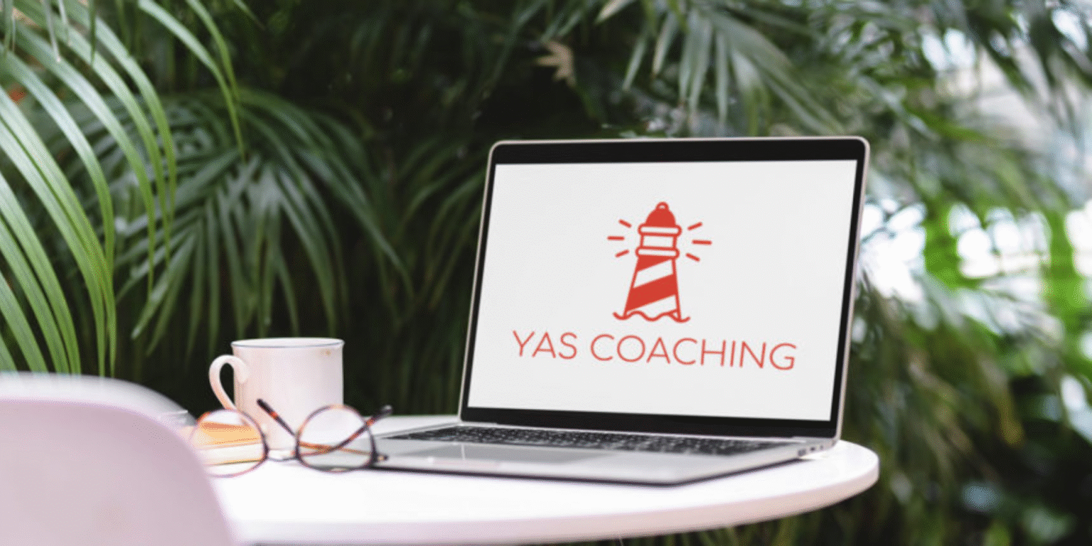 Yasmina Rauber: Leading with Purpose and Clarity Laptop on outdoor table displaying YAS Coaching lighthouse logo beside coffee cup and glasses, symbolizing Yasmina Rauber’s leadership coaching work.