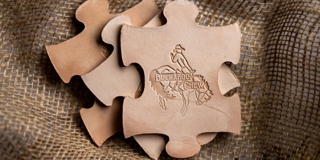 Puzzle-shaped leather pieces with the 'Buckaroo Chew' logo, symbolizing natural, safe teething toys for babies.