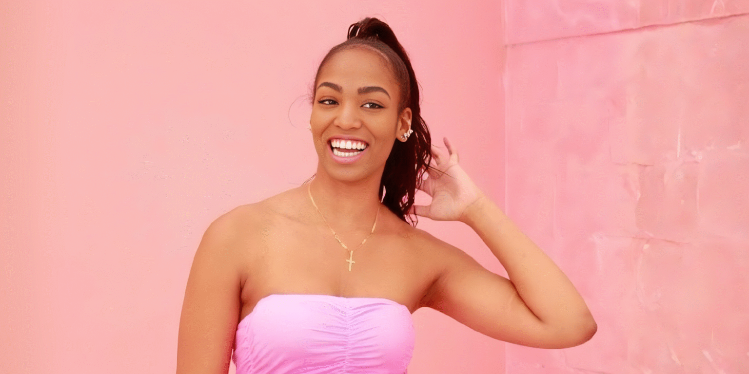 Kranay Jones smiling in a pink background, radiating positivity and empowerment.