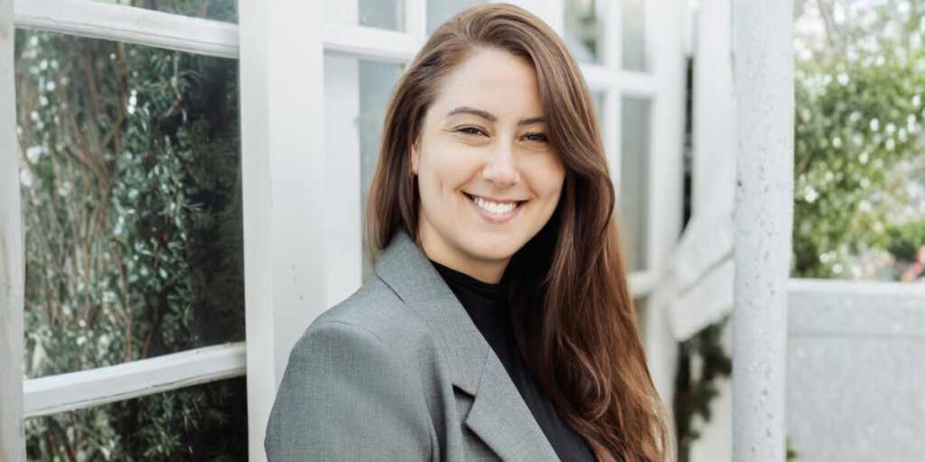 Tianna Mamalick, founder of SMB Marketing, smiling in front of windows, showcasing a calm, professional approach to business growth.