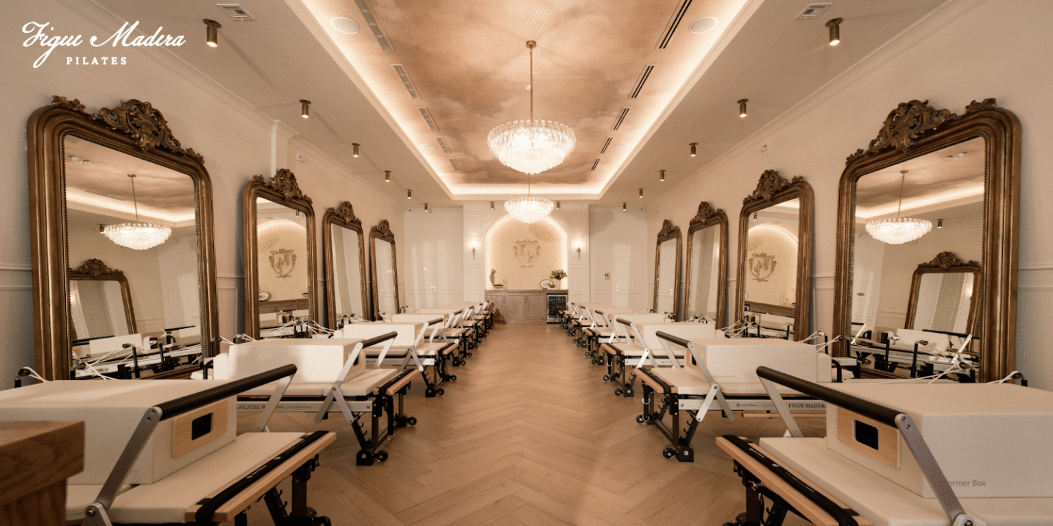 Elegant Pilates studio with reformers, chandeliers, and large mirrors for a serene atmosphere.