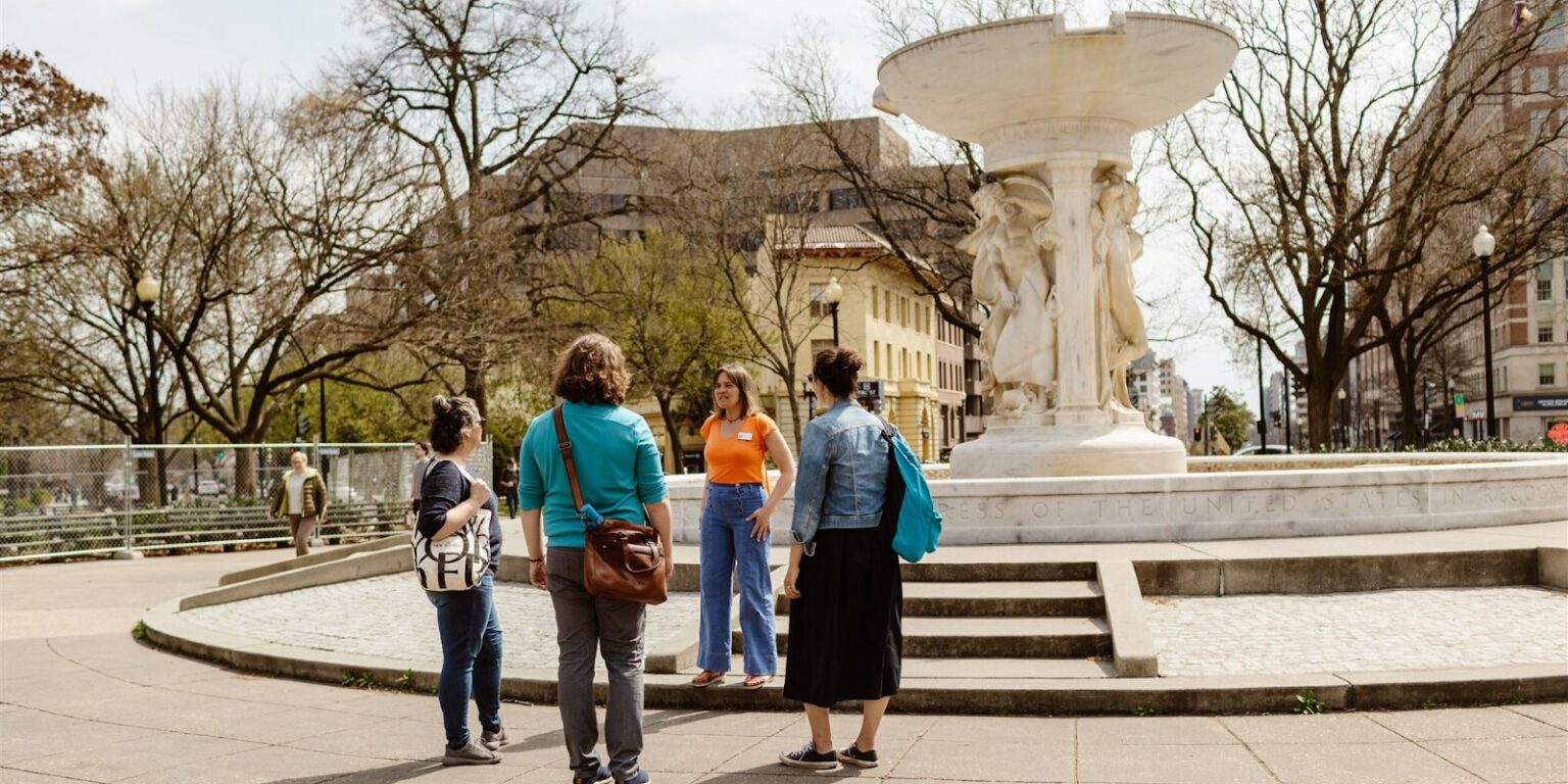 Three people stand around a city fountain, enjoying a moment of connection in an urban setting.