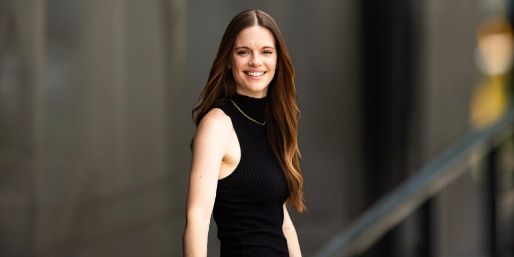 Elle Army is smiling, standing confidently outdoors in a black sleeveless turtleneck, showcasing a compassionate, professional demeanor.