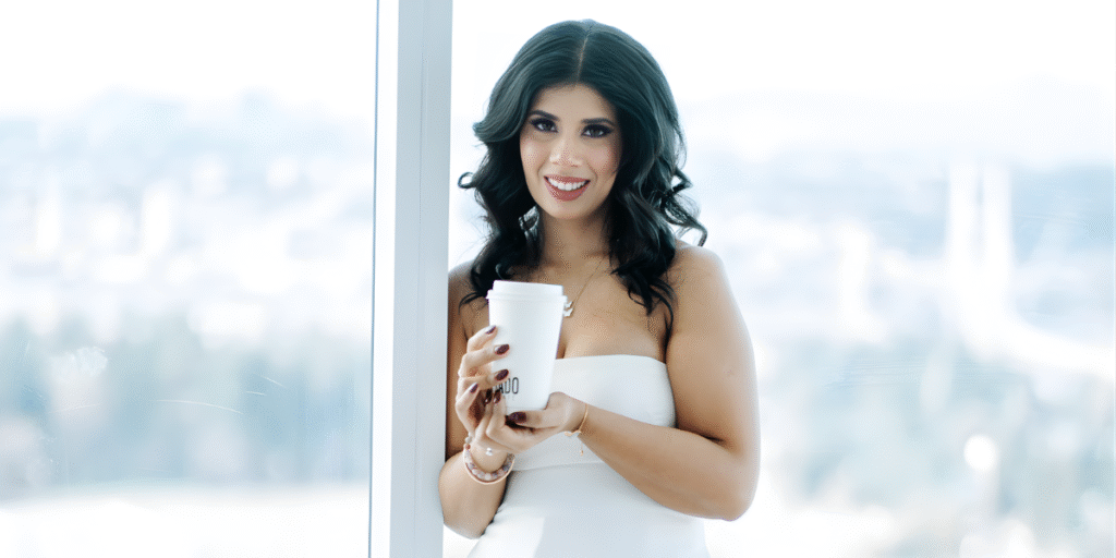 Priya Jhajj, founder of NeuroSomatics, standing confidently with a coffee cup in a bright, modern office, embodying a blend of science and holistic healing